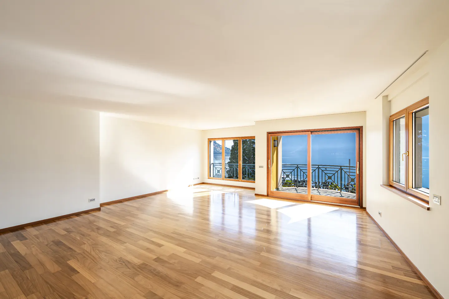 Bright, empty room with hardwood floors, white walls, and large windows with a view of the ocean.