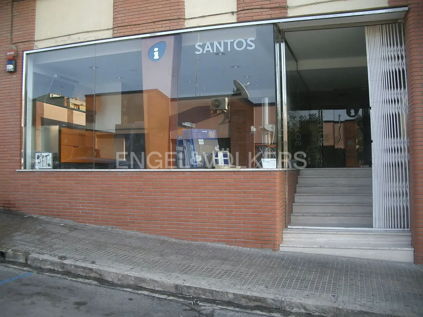 Exterior view of Engel & Volkers real estate office with brick facade, glass windows, and metal security gate. "Santos" is visible on the window.