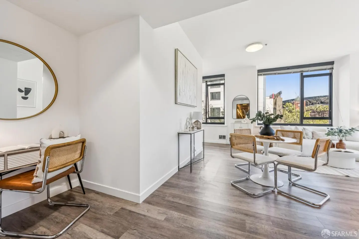 Bright, modern apartment interior with white walls, wood floors, and large windows. A round table with four chairs sits near a white sofa.