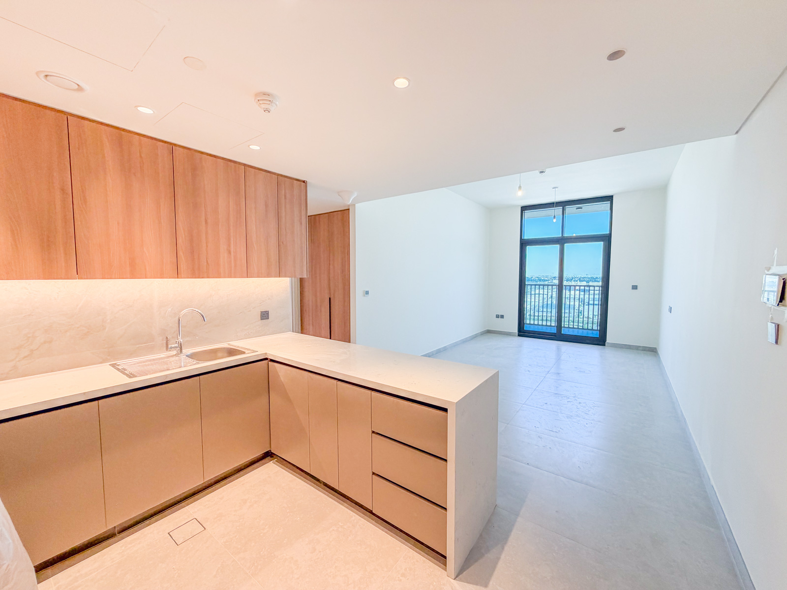 Modern kitchen with light wood cabinets, white countertops, and an open-plan living area with a balcony view. [AI-generated text]