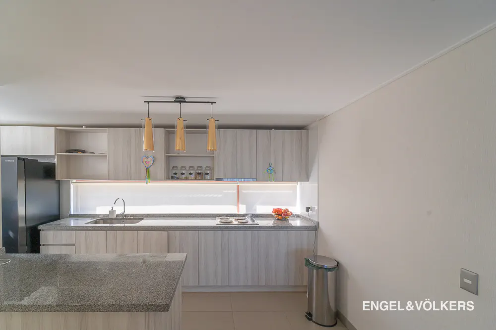 Bright kitchen with gray cabinets, granite countertops, and stainless steel trash can. Three pendant lights hang above the sink.