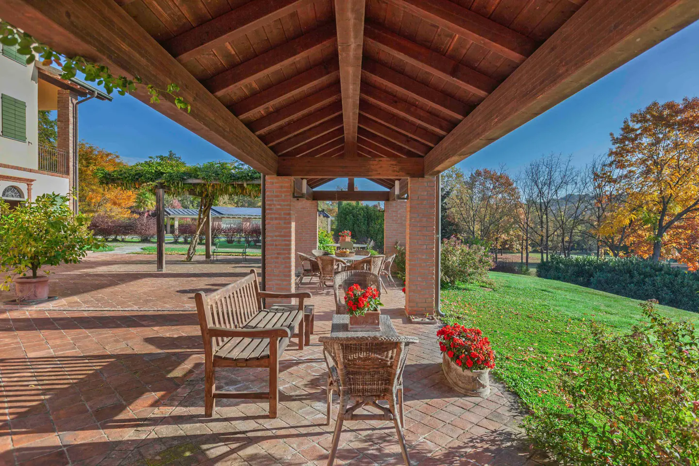 Covered patio with brick floor, wooden beams, and furniture. A green lawn and trees are visible in the background.
