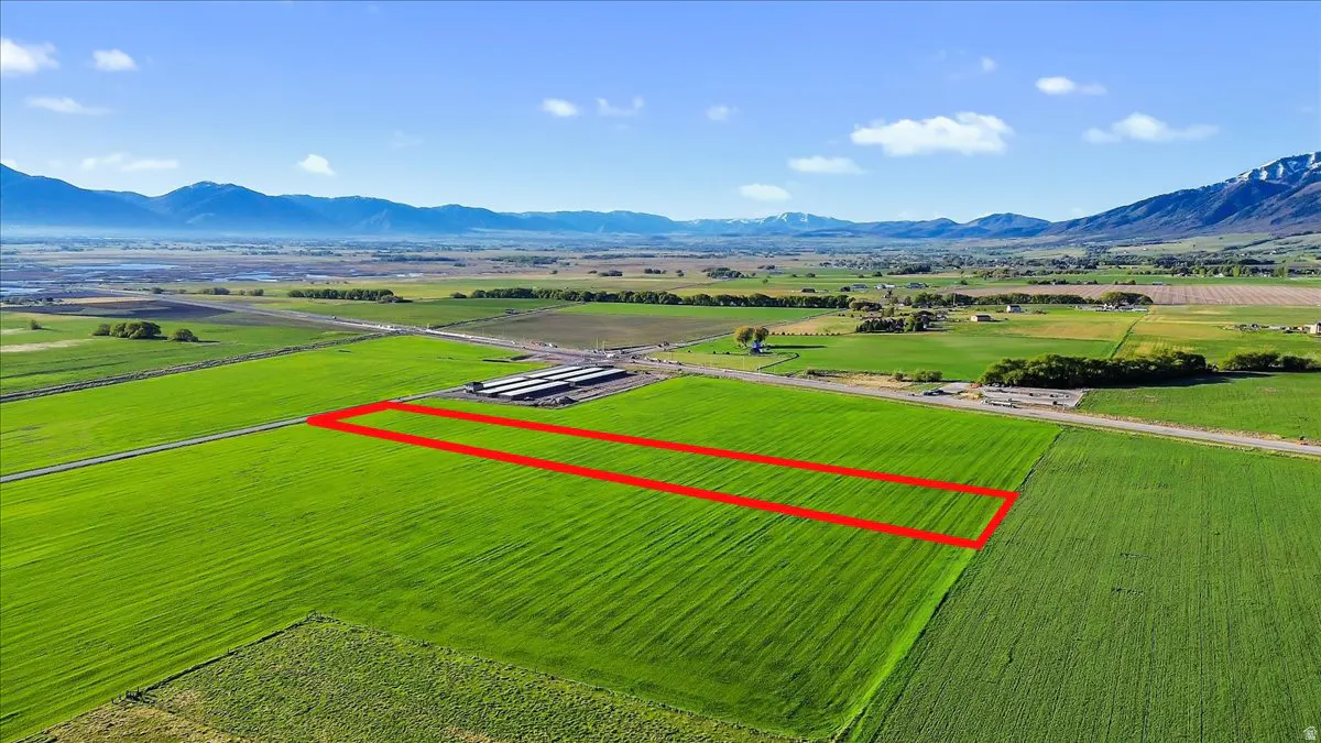 Aerial view of a green field outlined in red, with mountains and a blue sky in the background.