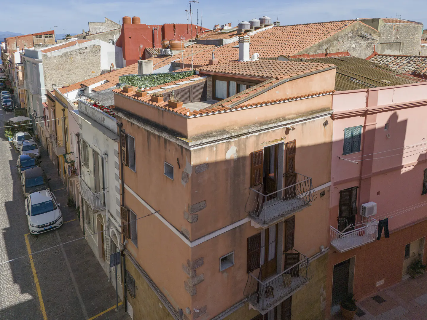 Aerial view of a peach-colored building with balconies and brown shutters, surrounded by other buildings with red tile roofs.