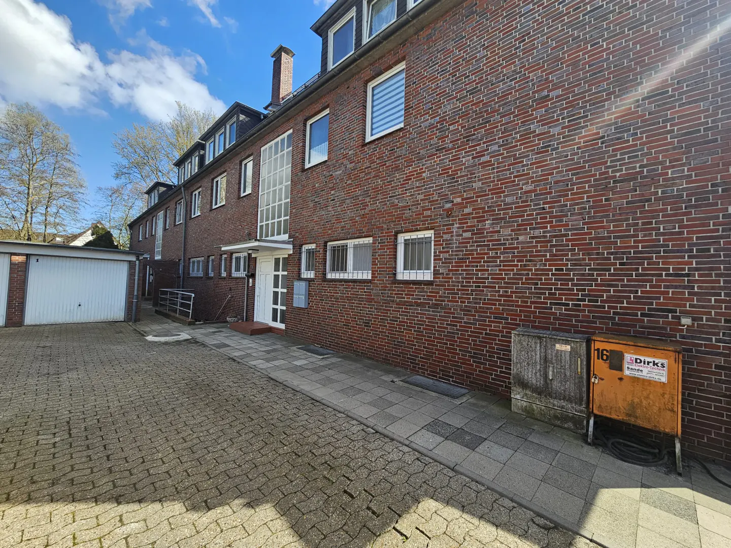 Exterior view of a red brick apartment building with white trim and a white garage on a paved driveway.