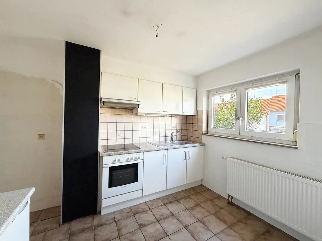 Bright kitchen with white cabinets, oven, sink, and window. Beige tile floor and backsplash. Black accent wall.