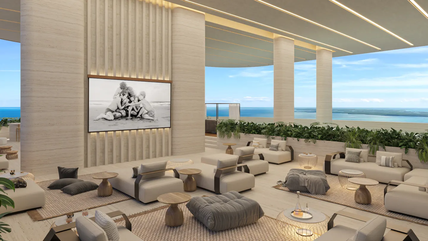 Luxury outdoor lounge with cream seating, wood tables, and a large black and white photo on the wall. Ocean view in the background.