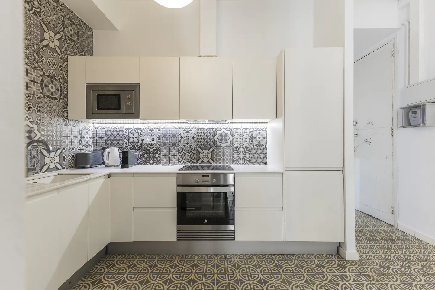 A modern kitchen with white cabinets, stainless steel appliances, and patterned backsplash and floor tiles.