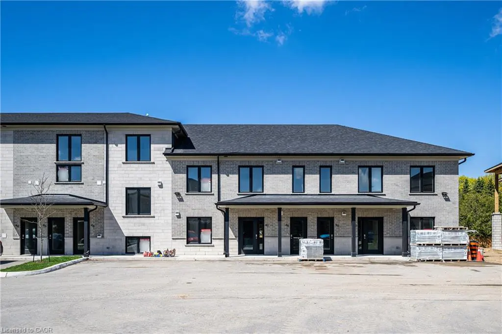 Exterior view of a two-story townhouse with light gray brick, black windows, and a dark gray roof under a clear blue sky.