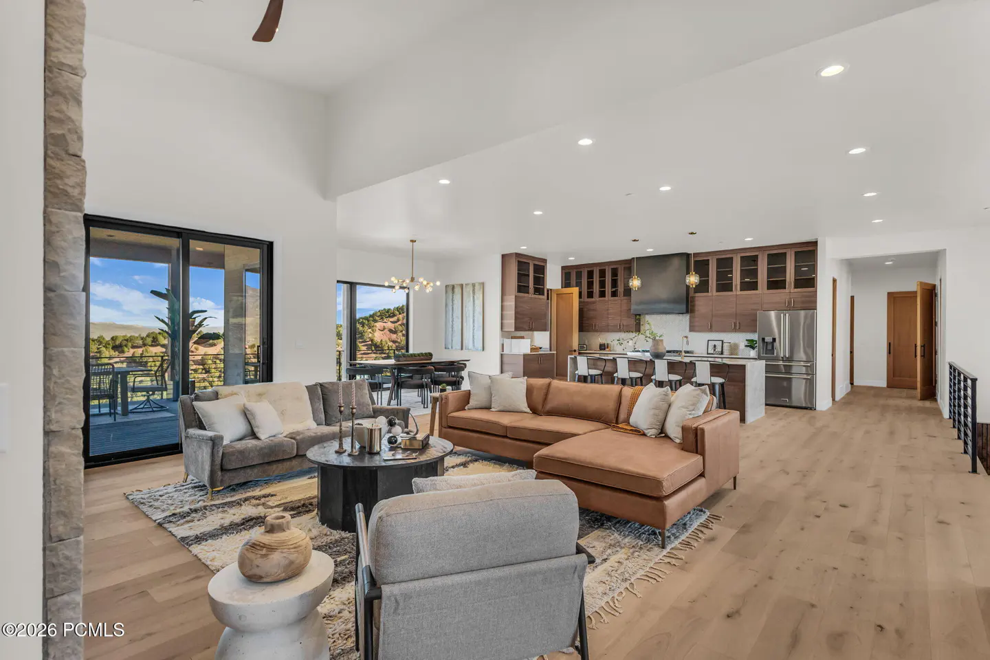 Open-concept living space with brown leather sofa, gray sofa, kitchen with wood cabinets, and a view of the mountains.