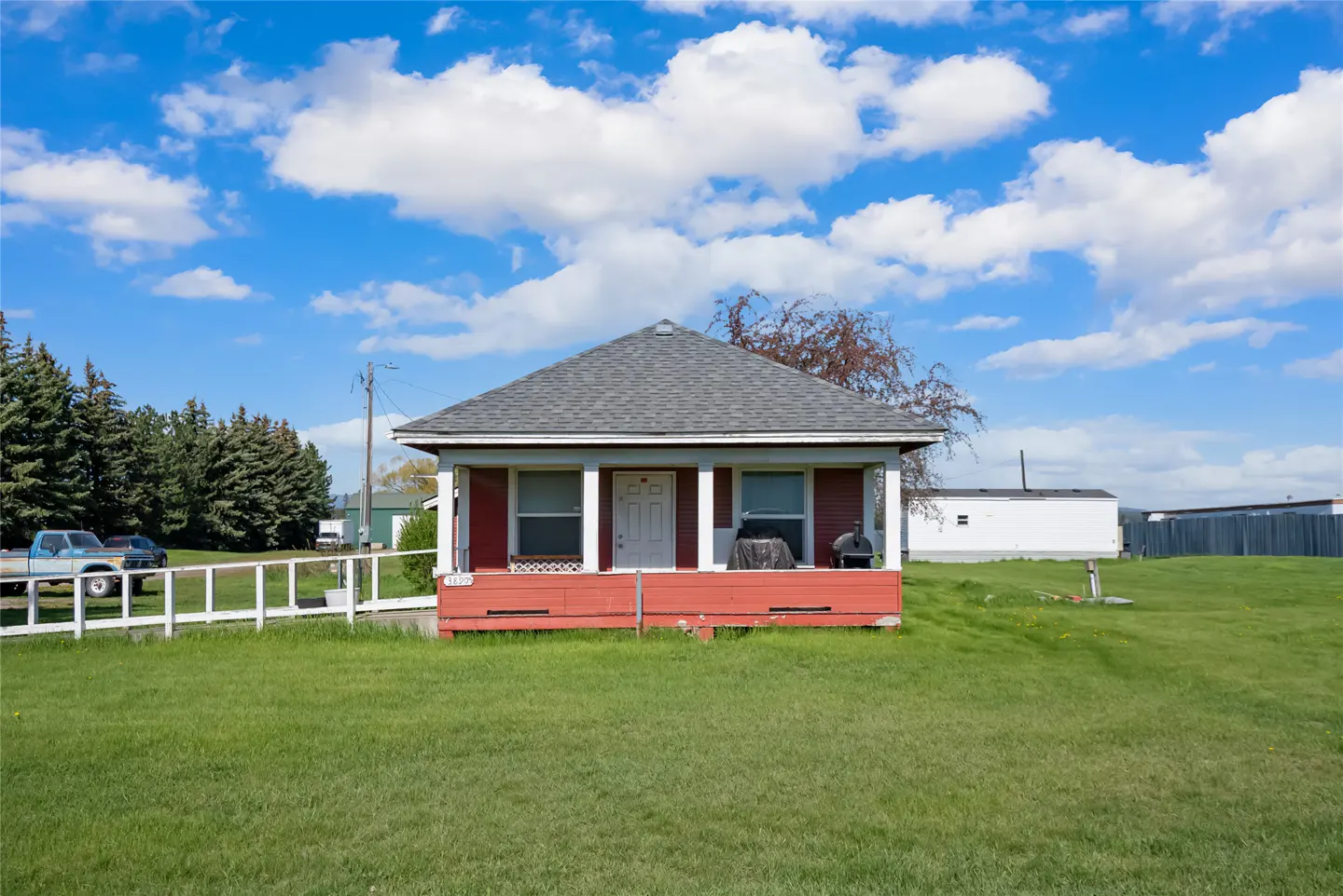 A small, red house with a gray roof sits on a green lawn under a blue, cloudy sky.