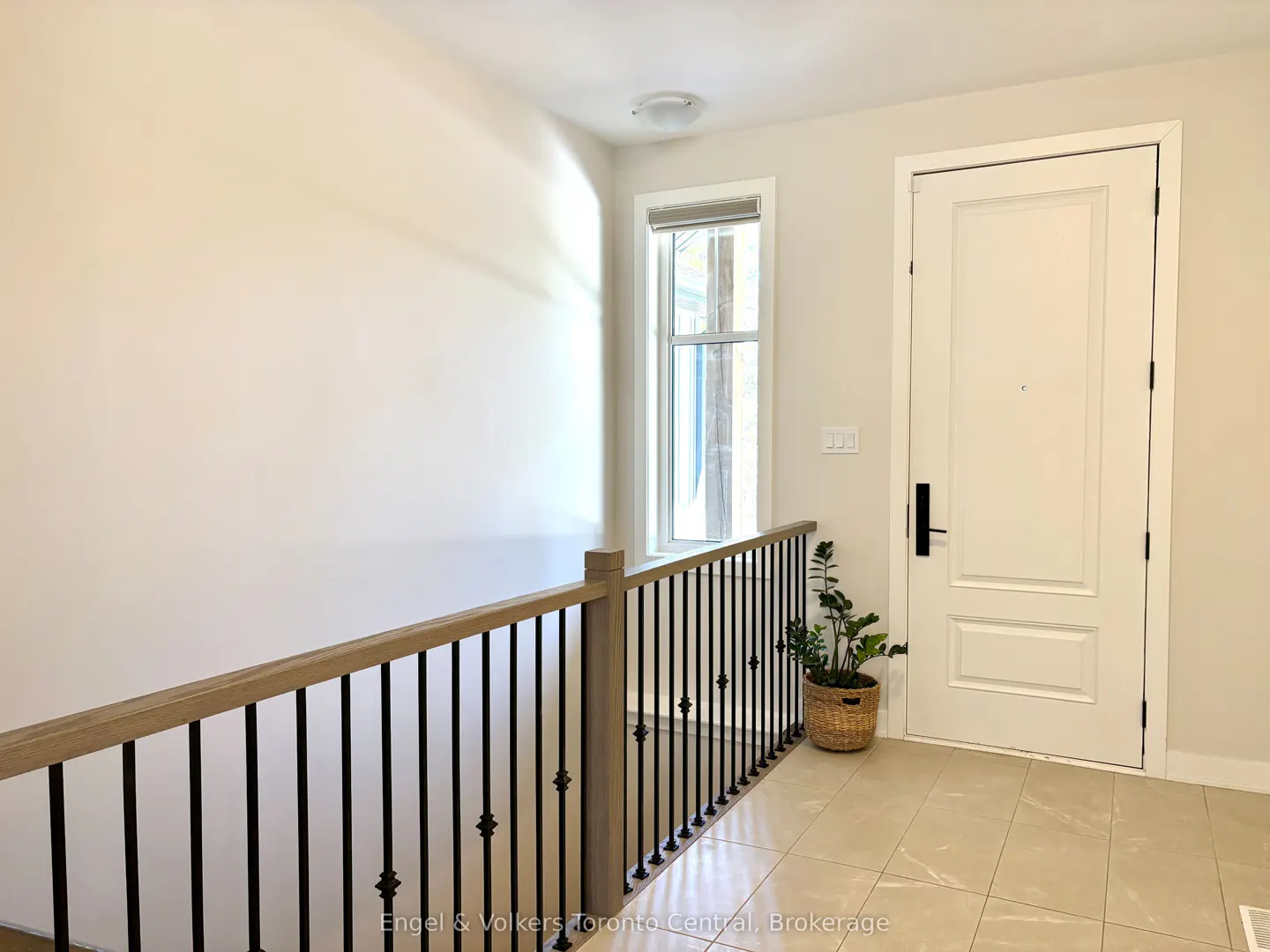 Entryway with a white door, black hardware, a window, and a wood and black railing. A potted plant sits near the door.
