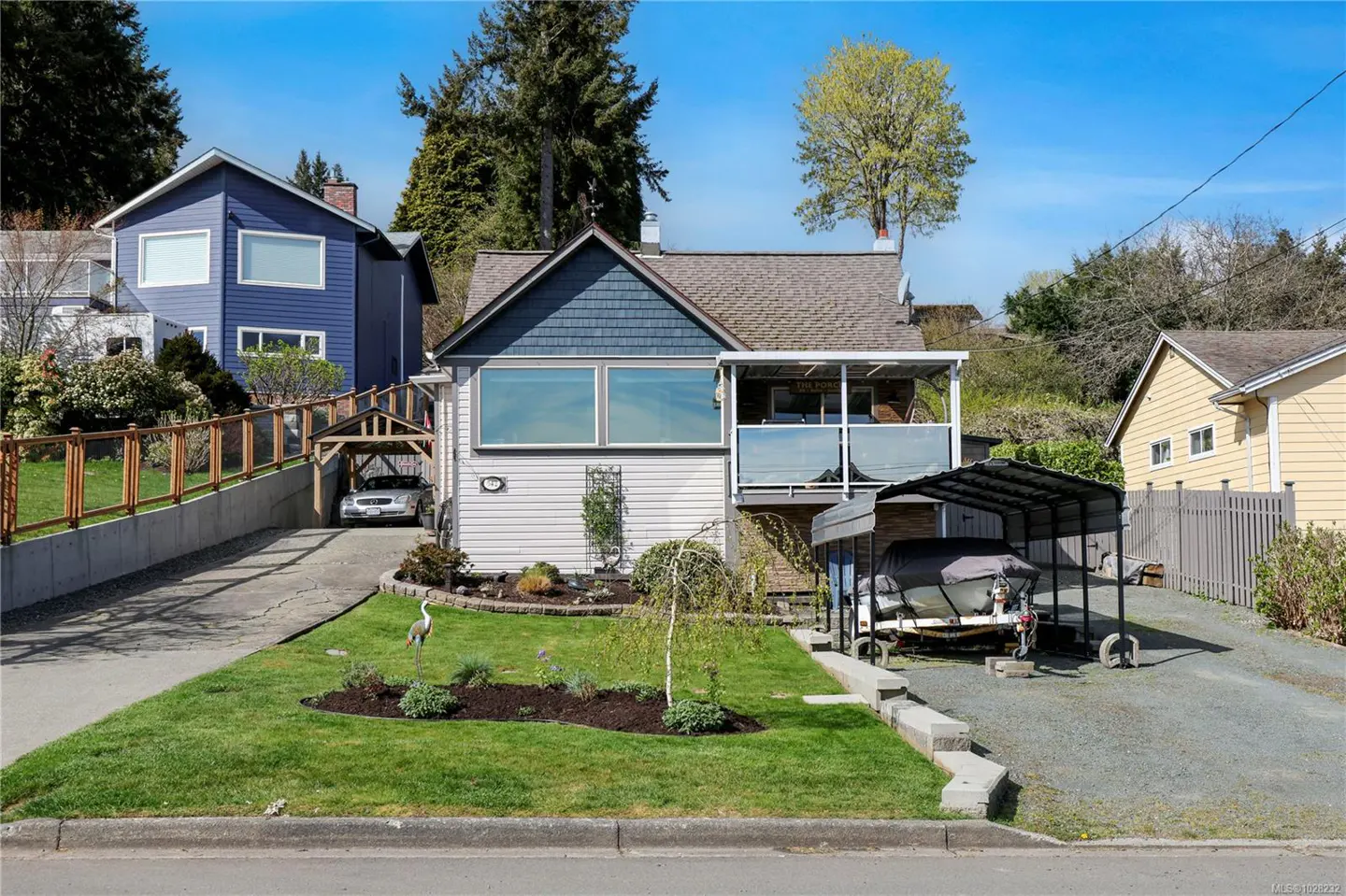 A two-story house with a blue roof and white siding, a car in the driveway, and a boat under a carport.