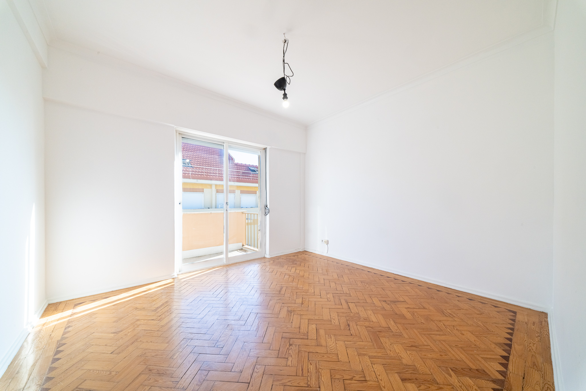 Empty room with white walls, herringbone wood flooring, and a sliding glass door leading to a balcony. [AI-generated text]