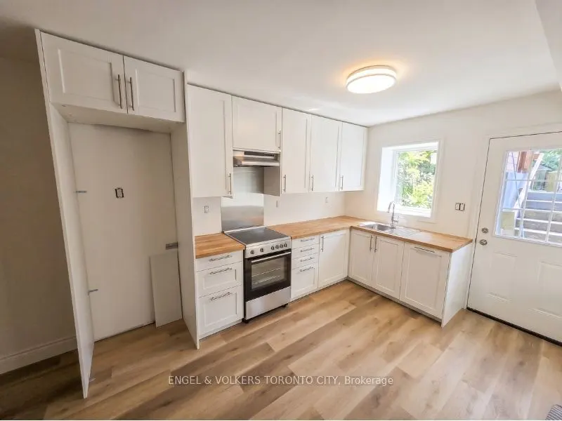 Modern kitchen with white cabinets, wood countertops, stainless steel stove, and light wood flooring.