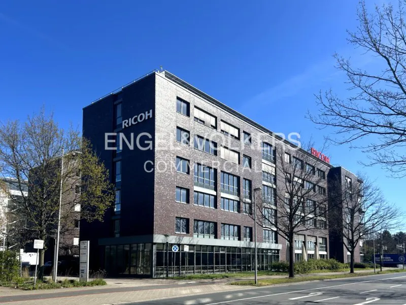 Exterior of a brick commercial building with "Ricoh" and "Engel & Volkers Commercial" signs under a blue sky.