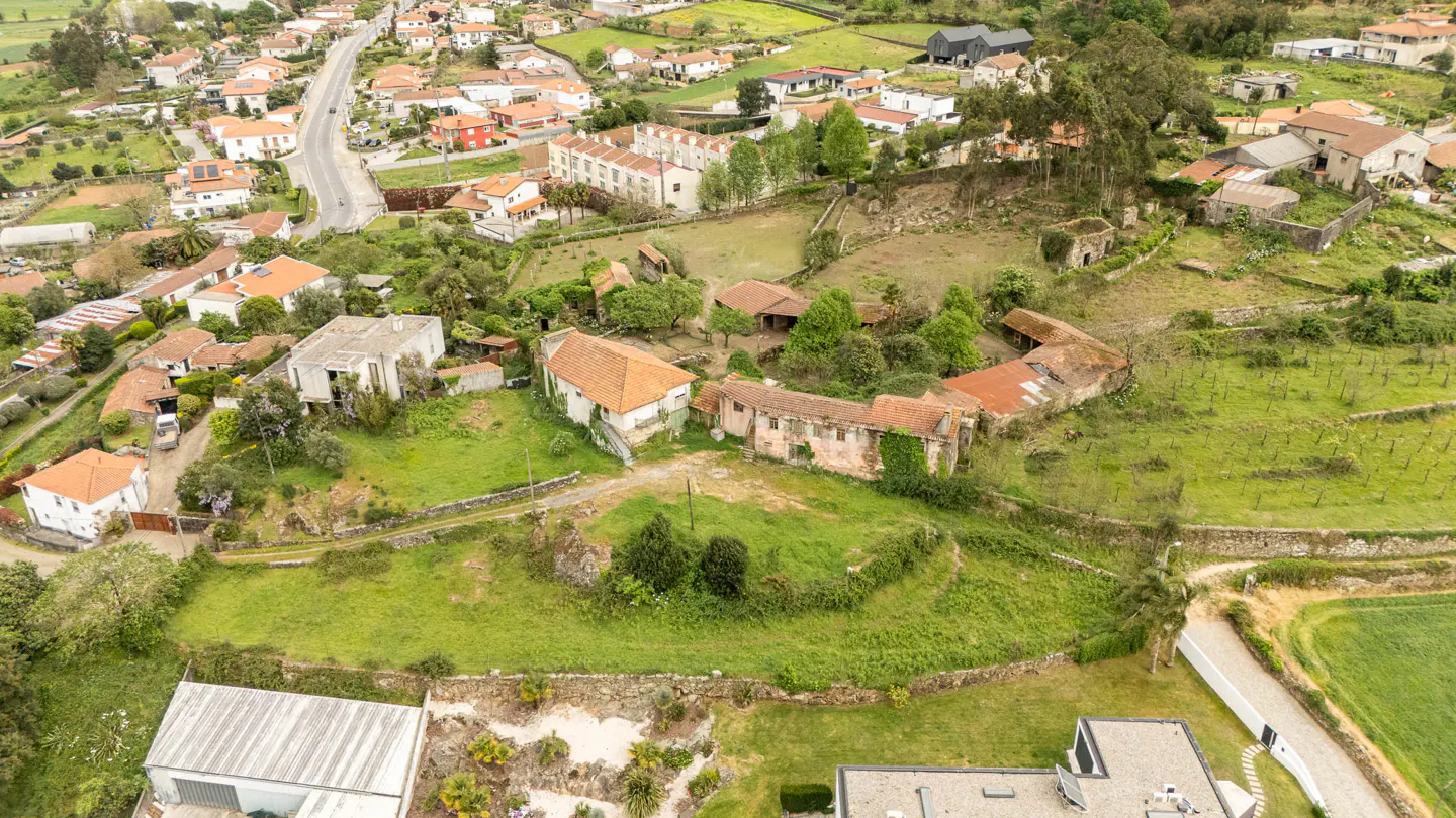 Aerial view of a rural property with stone buildings, green grass, and orange tile roofs in a village setting.