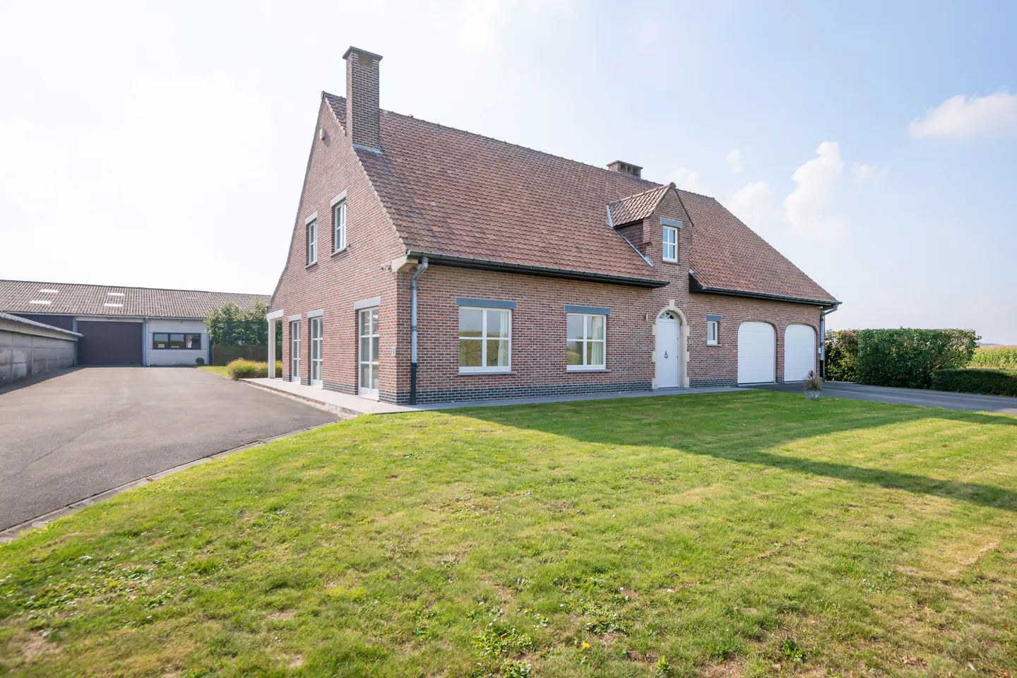 Brick house with a red tile roof, white trim, and a green lawn on a sunny day.