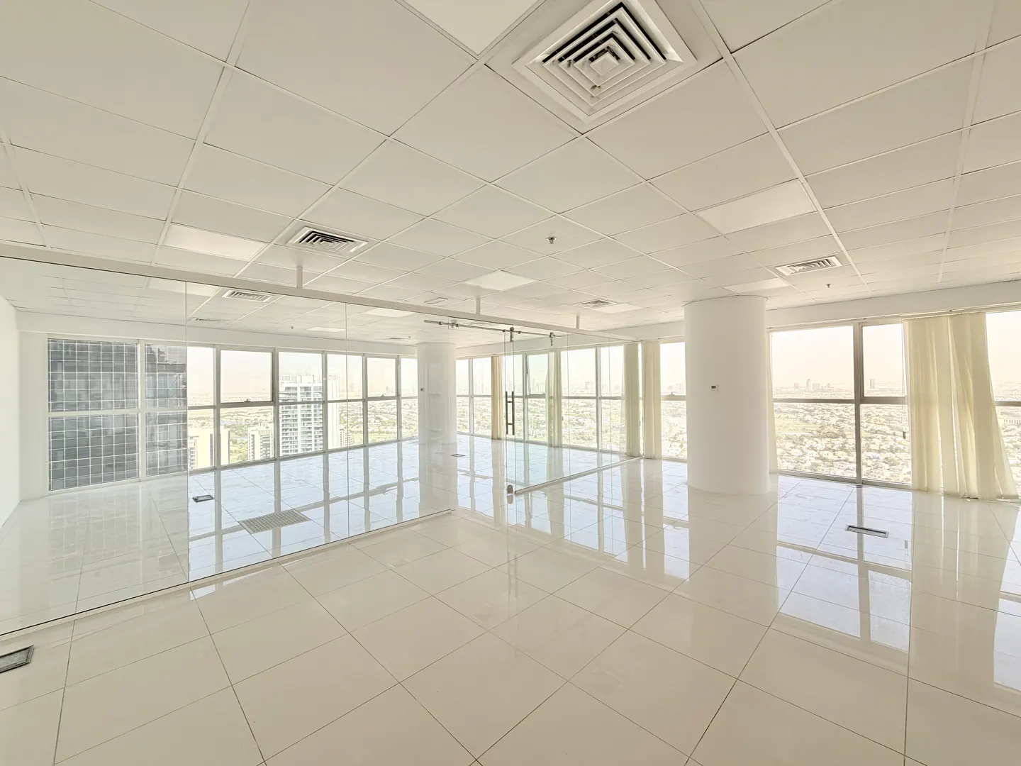 Bright, empty office space with white tile floors and large windows overlooking a city.