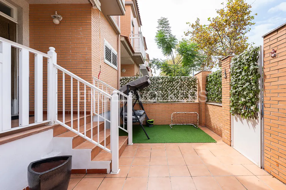 Small brick patio with white railings, a hanging swing chair, a small soccer goal on artificial grass, and ivy wall decor.