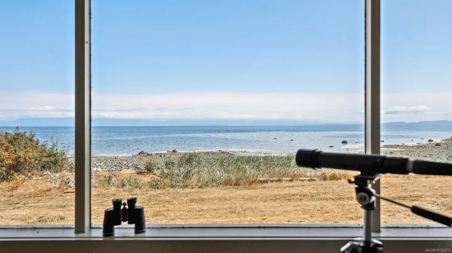 Ocean view from a window with binoculars and a telescope in the foreground. The sky is blue and the water is calm.
