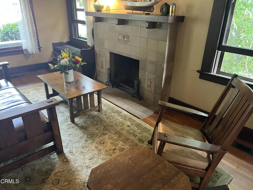 Living room with a tiled fireplace, wooden furniture, and a patterned rug. A vase of flowers sits on the coffee table.