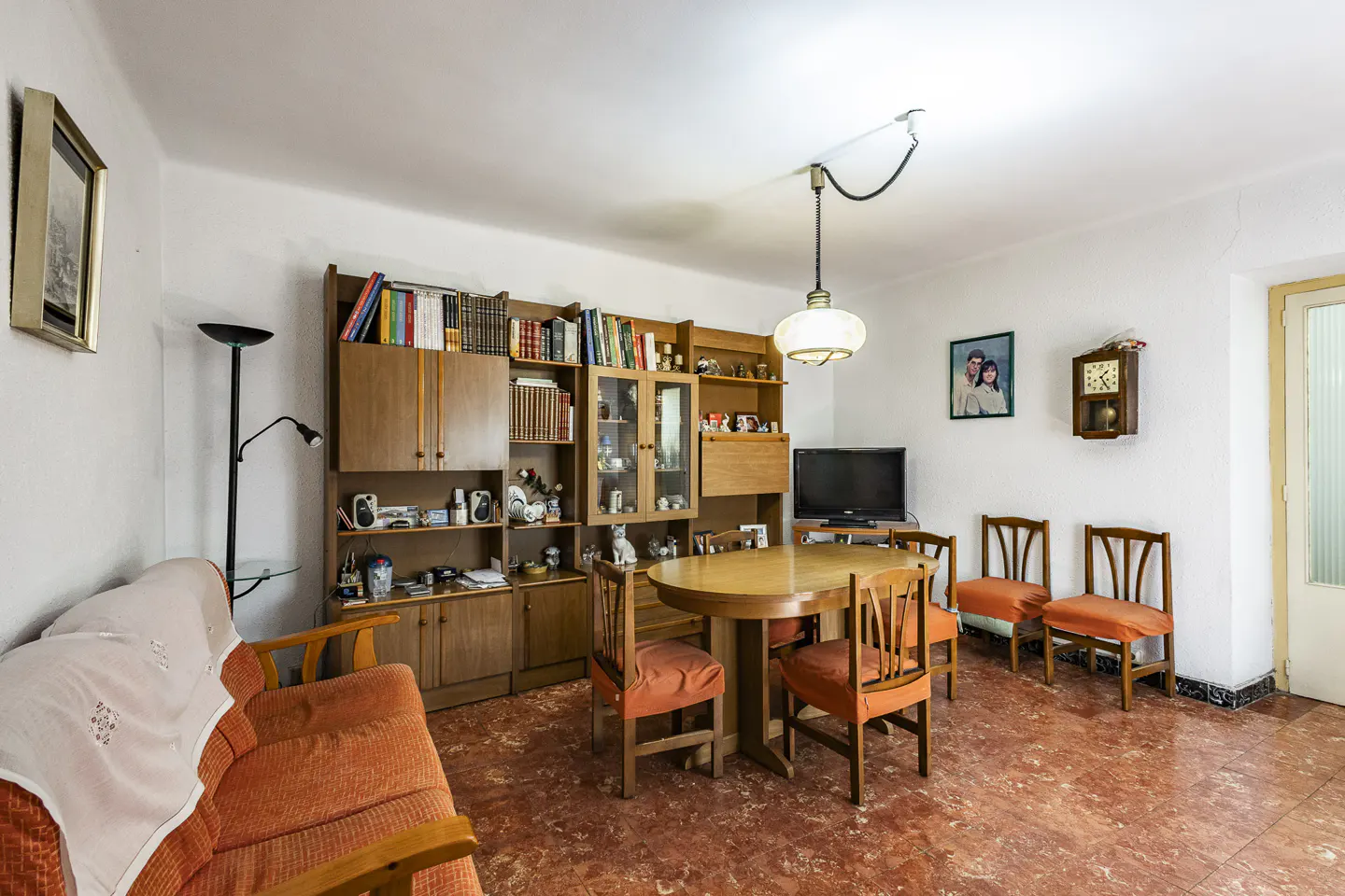 Living room with orange sofa, wooden dining set, and built-in bookcase. A vintage pendant light hangs above the table.