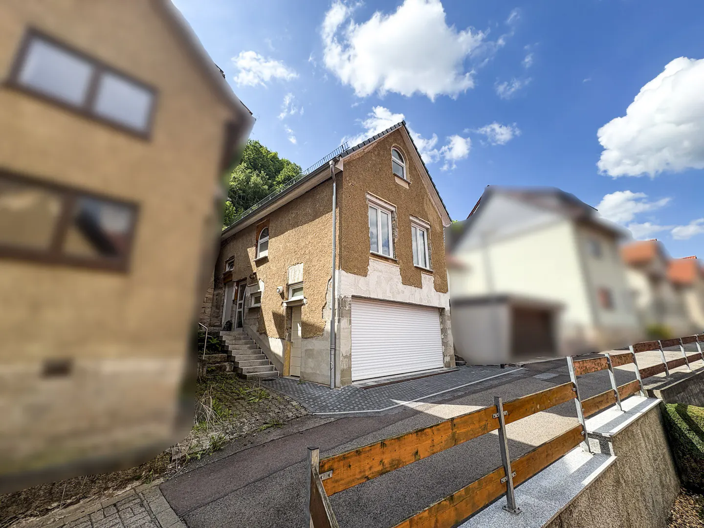 Exterior view of a two-story stucco house with a white garage door and a stairway to the side entrance. Blue sky with clouds.