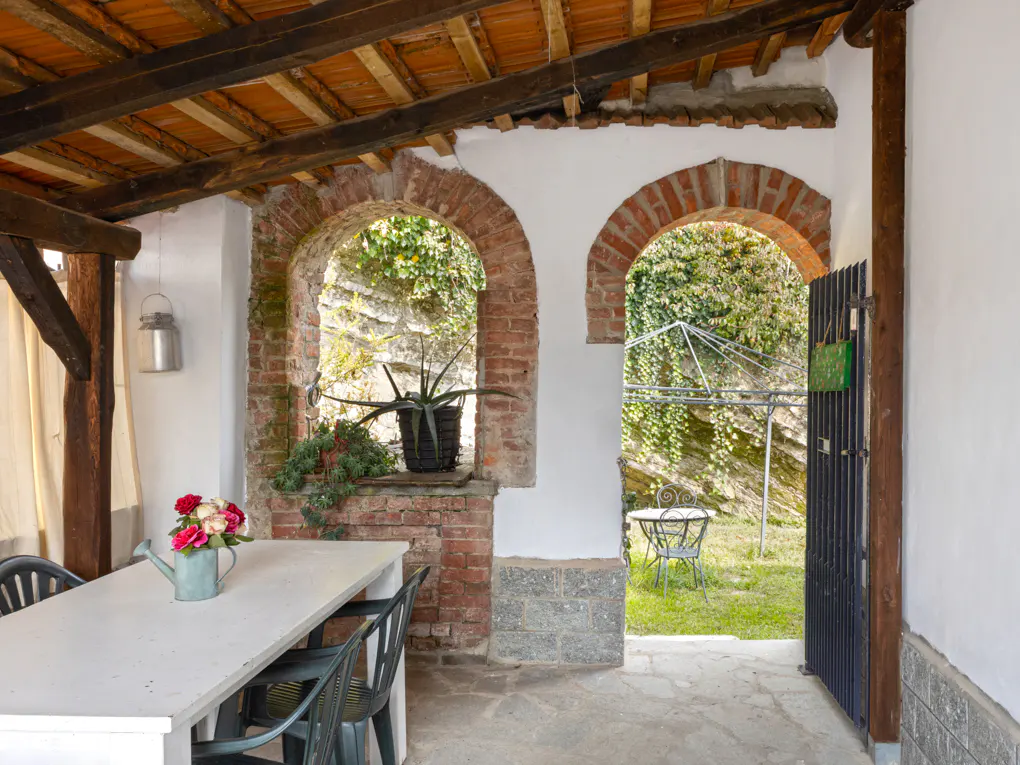 Covered patio with brick arches, a white table with flowers, and a view of a green lawn with a table and chairs.