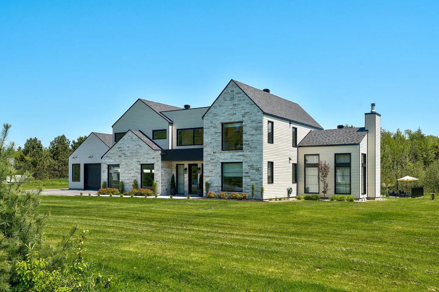 A modern two-story house with stone and white siding, black window frames, and a green lawn under a blue sky.
