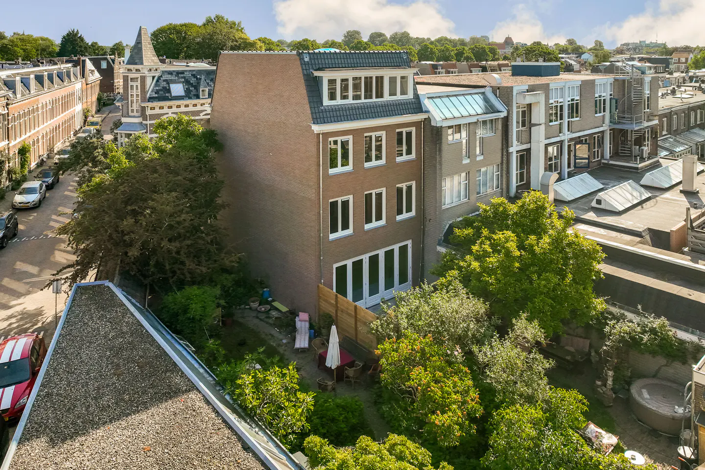Aerial view of a multi-story brick townhouse with a private garden, patio furniture, and surrounding urban neighborhood.