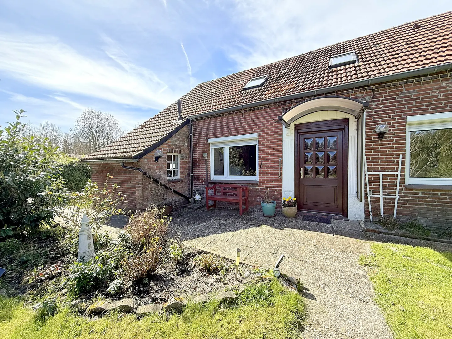 Exterior of a brick house with a brown front door and a red bench in front of a window.
