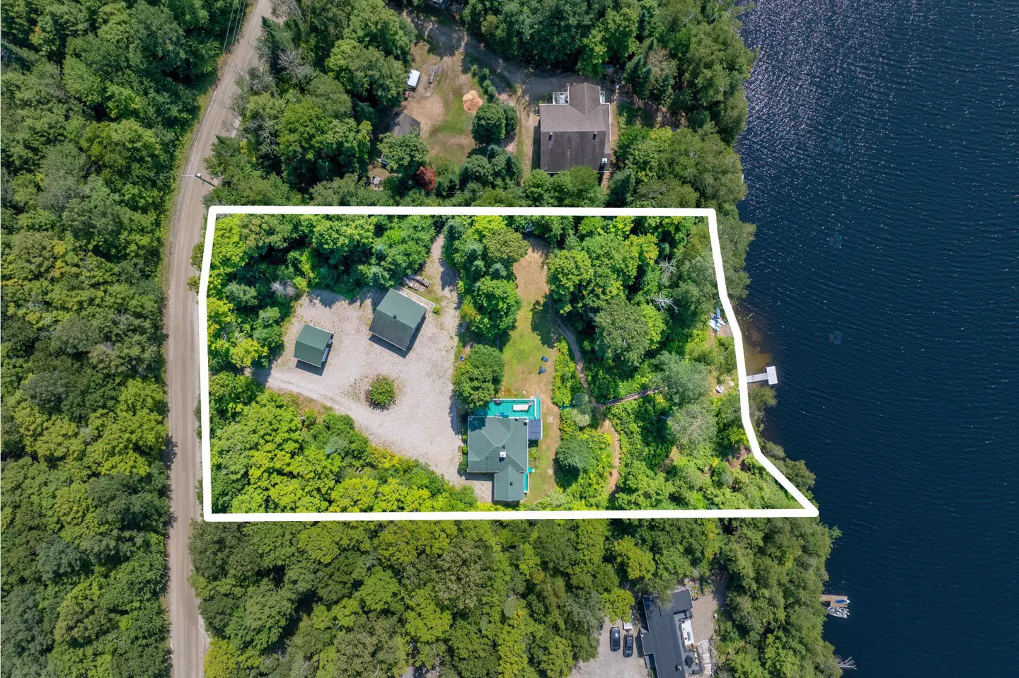 Aerial view of a wooded waterfront property outlined in white, featuring a house, two outbuildings, and a private dock.