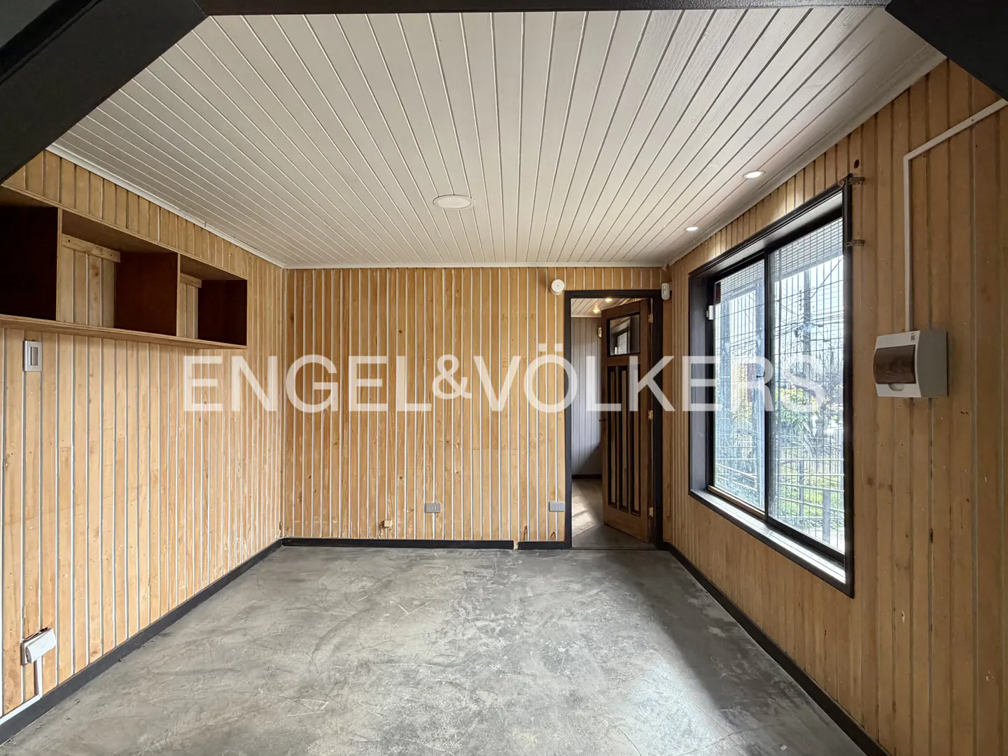 Empty room with light wood-paneled walls, a white slatted ceiling, concrete floor, and a window looking outside.