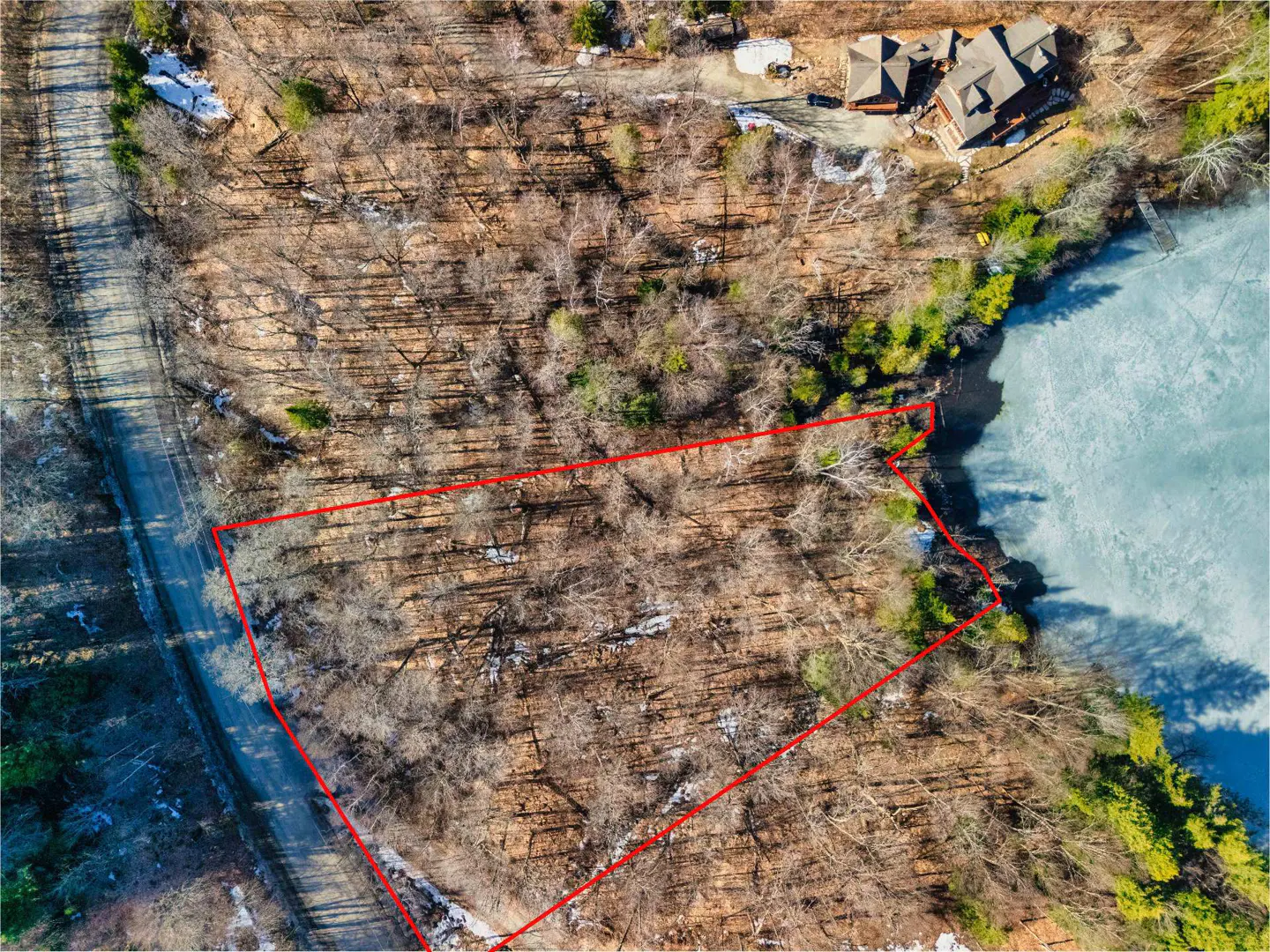 Aerial view of a wooded lot outlined in red, adjacent to a frozen lake and a house.
