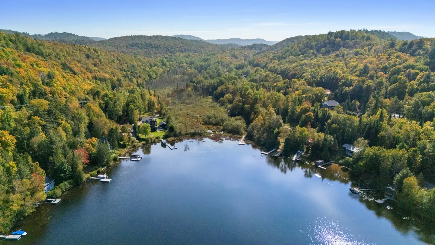 Aerial view of a blue lake surrounded by green and yellow trees, with houses and docks along the shoreline.
