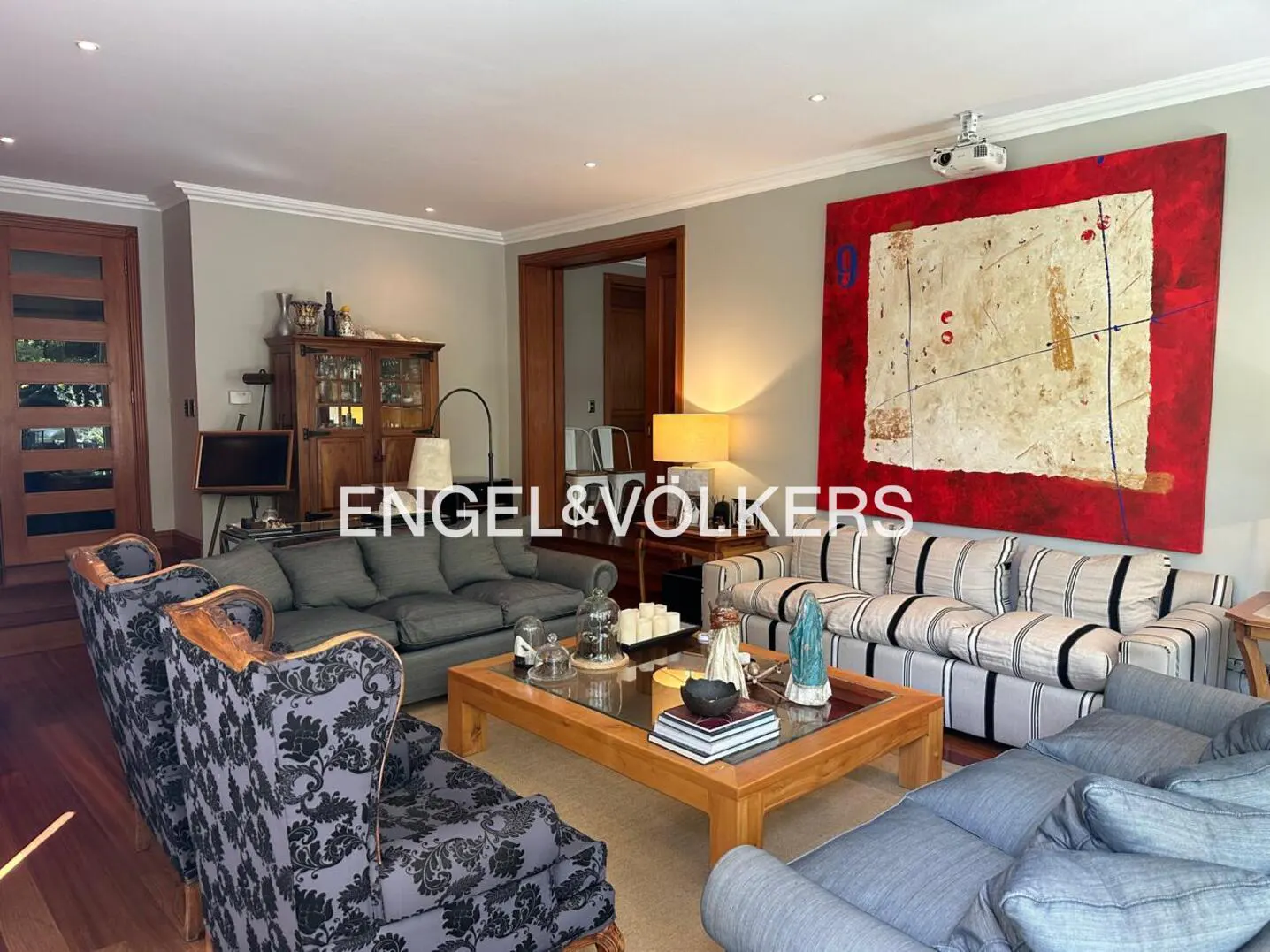 Living room with sofas, armchairs, and a wooden coffee table. A large red painting hangs on the wall. Engel & Völkers logo is visible.
