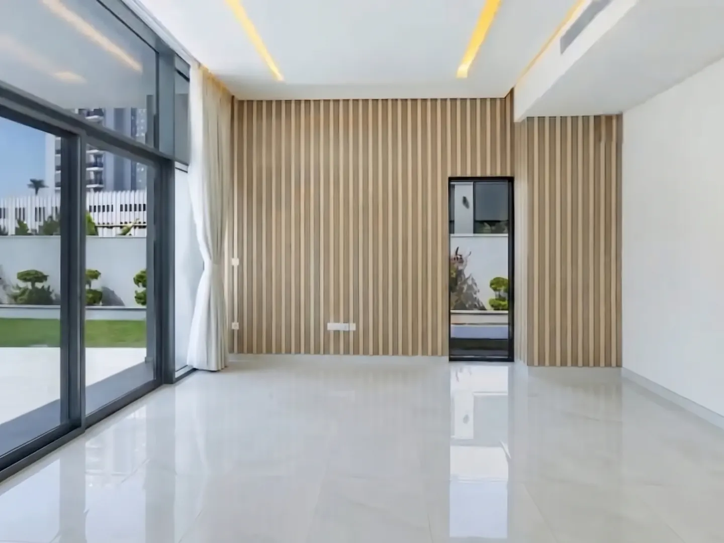 Bright, empty room with white tile floor, wood slat wall, and large glass doors to a green lawn.
