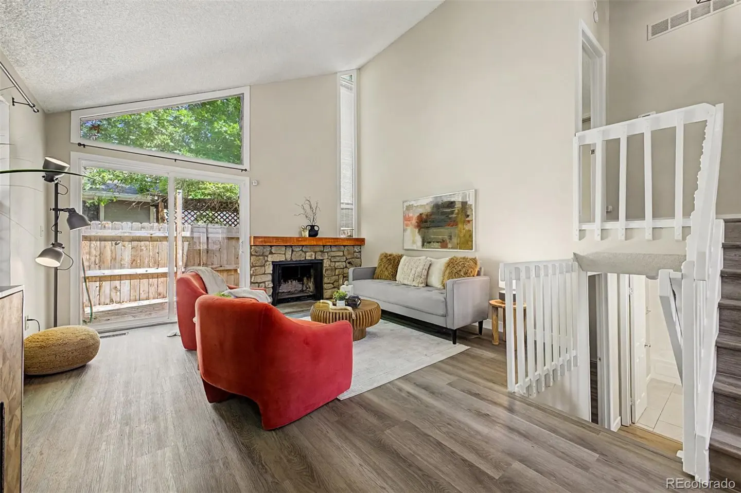 Living room with vaulted ceilings, stone fireplace, two red armchairs, grey sofa, and stairs with white railings.
