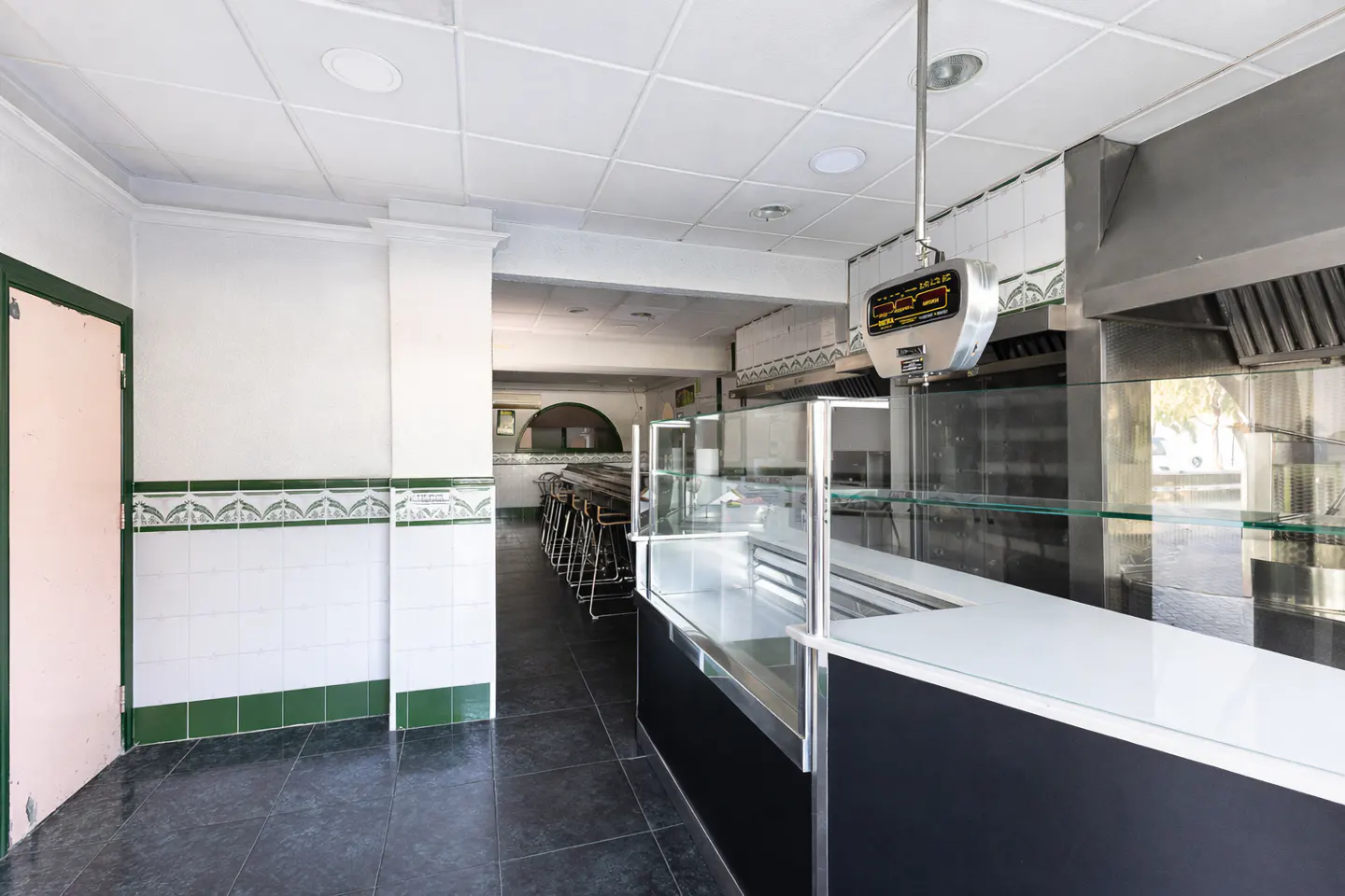 Empty restaurant interior with black tile floors, white walls, and a long counter with glass display cases.