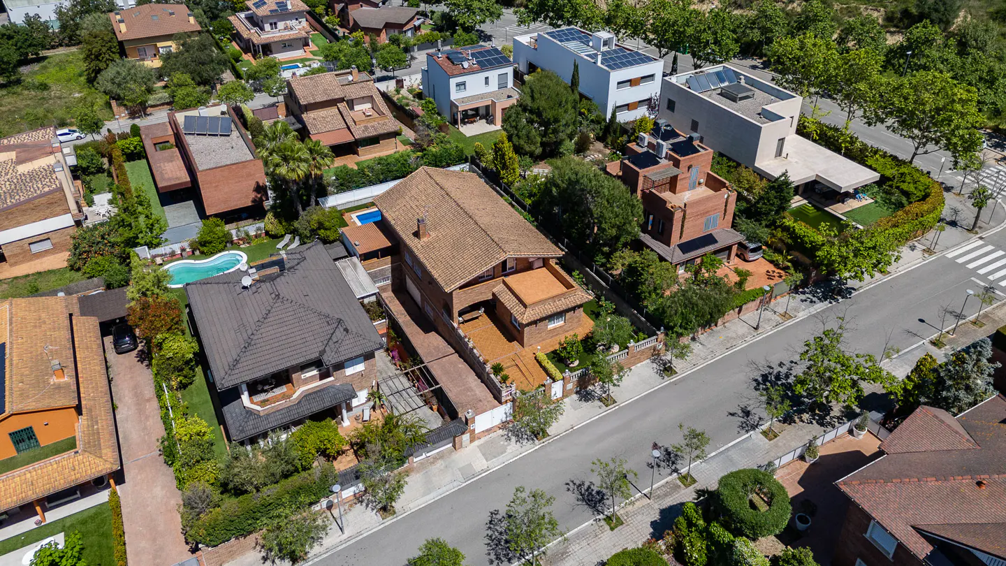 Aerial view of a residential neighborhood with various houses, trees, and a street with a crosswalk.