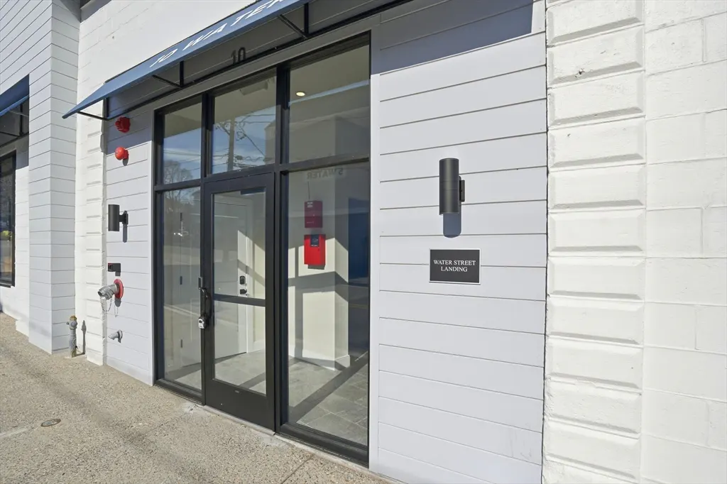 Exterior view of Water Street Landing with black framed glass doors and white siding. A black awning is above the door.