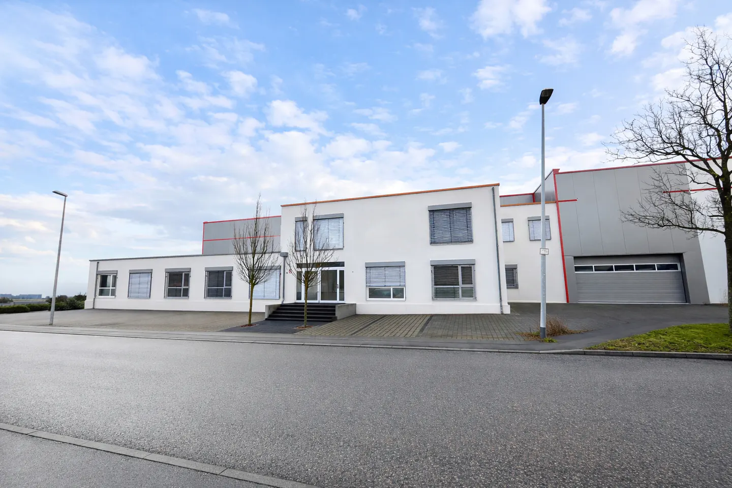 Modern white commercial building with gray accents, a large garage door, and a paved parking area under a cloudy sky.