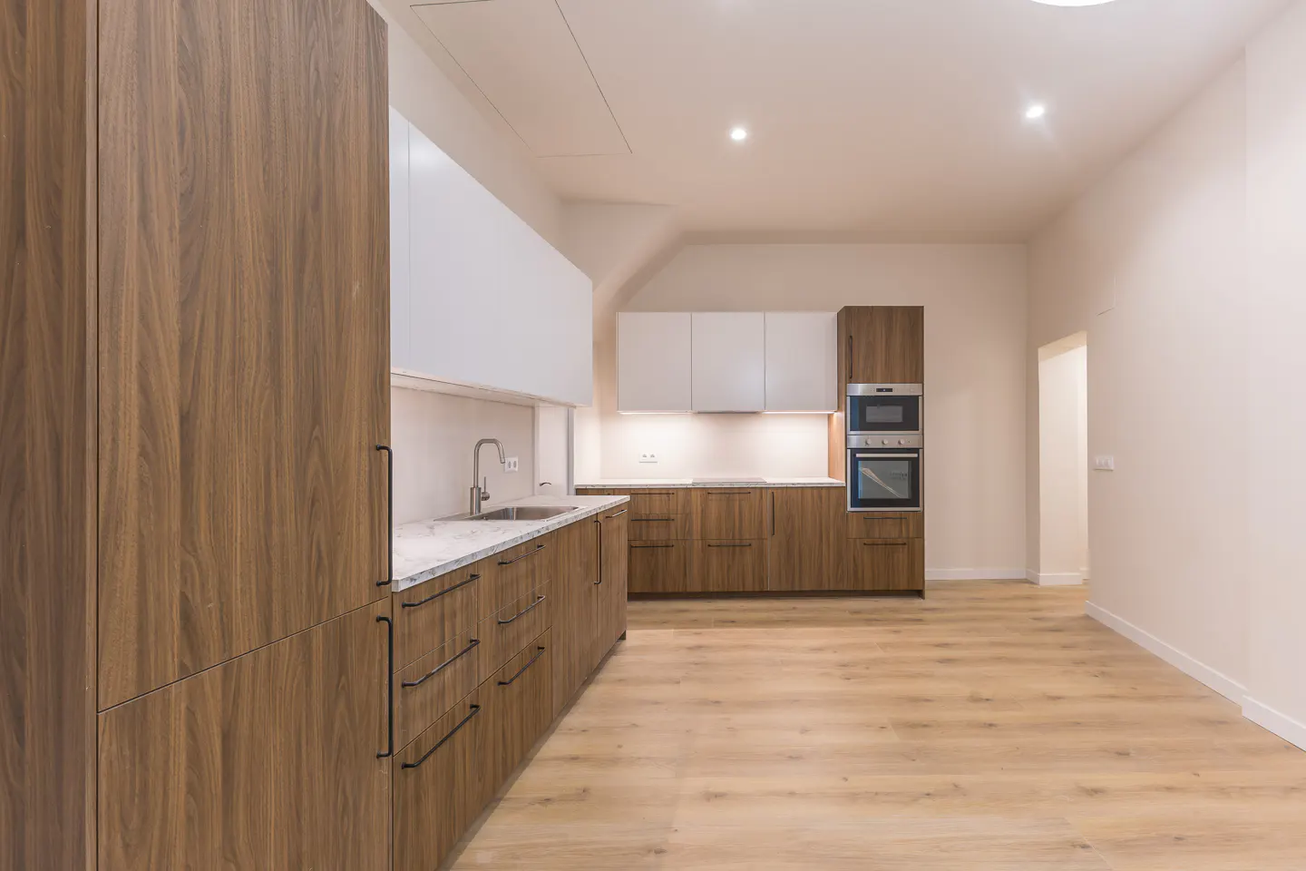 A modern kitchen with wood cabinets, white upper cabinets, marble countertops, and stainless steel appliances. The floor is light wood.