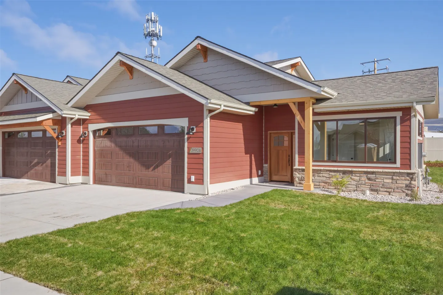Exterior of a red, single-story home with a brown garage door, wood door, and green lawn. A cell tower is visible in the background.