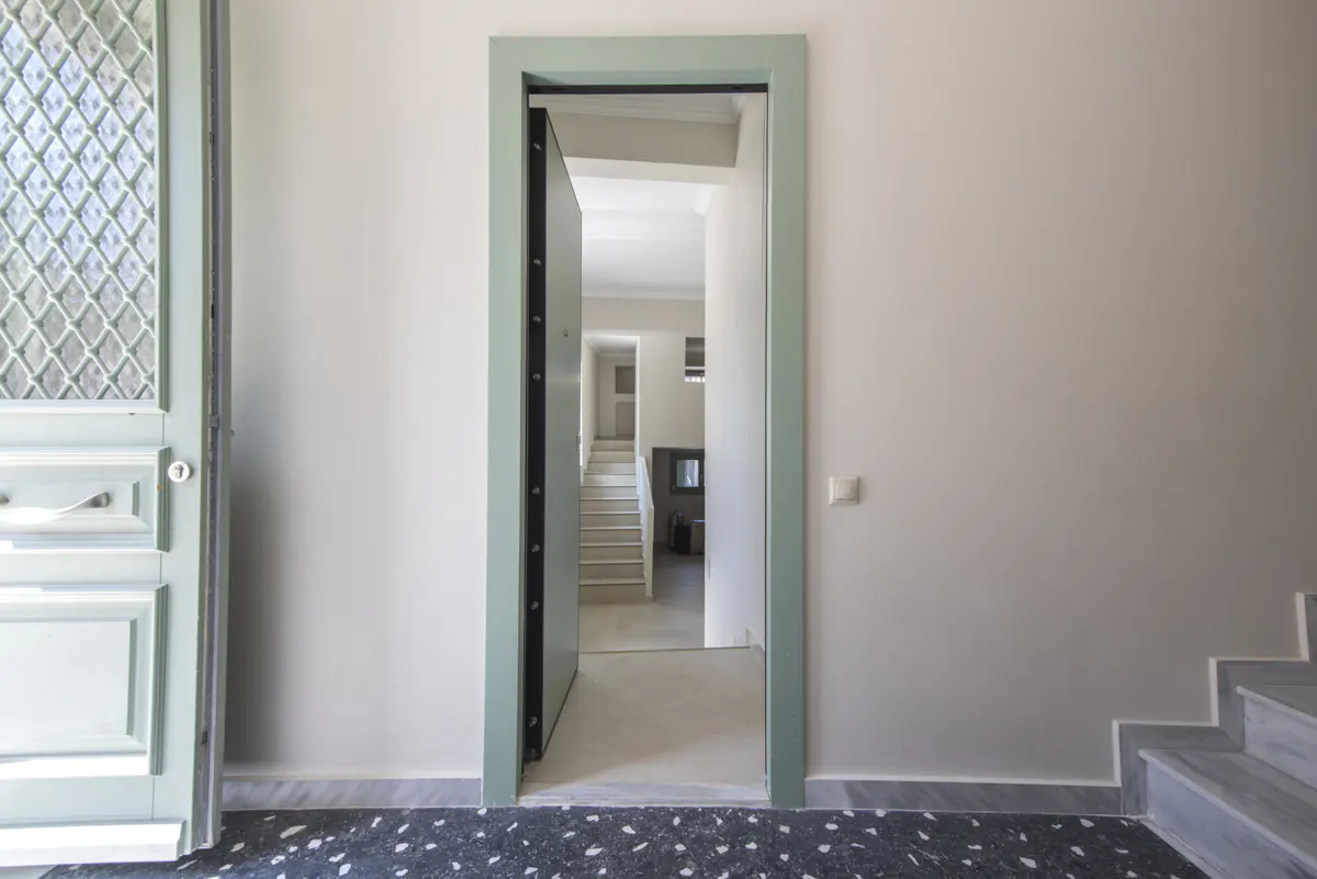 Interior view of a home with an open, light-green door frame. A staircase is visible through the doorway. A patterned door is to the left.