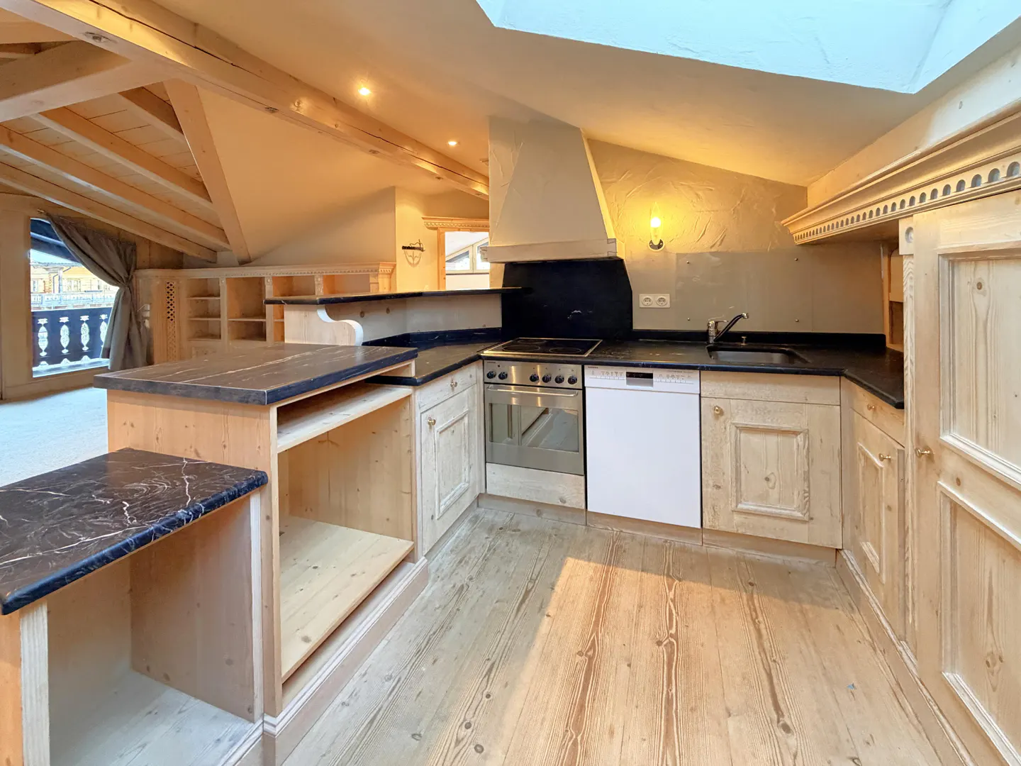 A bright kitchen with wood cabinets, black countertops, and wood floors. A skylight is visible.