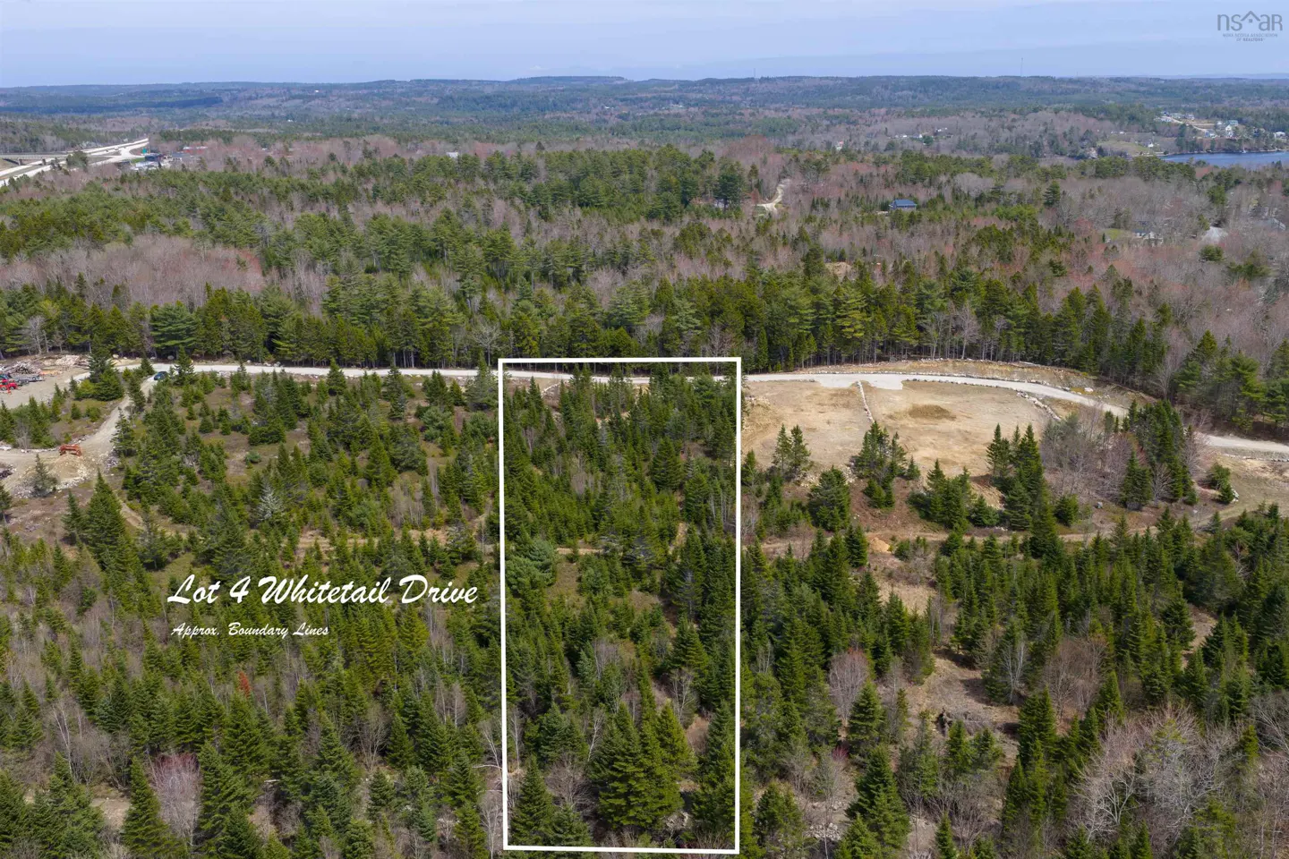 Aerial view of Lot 4 Whitetail Drive, a wooded property outlined in white, surrounded by green trees and a distant landscape.