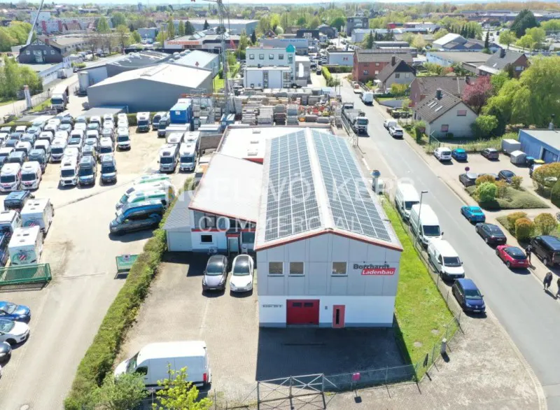 Aerial view of a commercial building with solar panels, surrounded by parked vehicles and greenery.