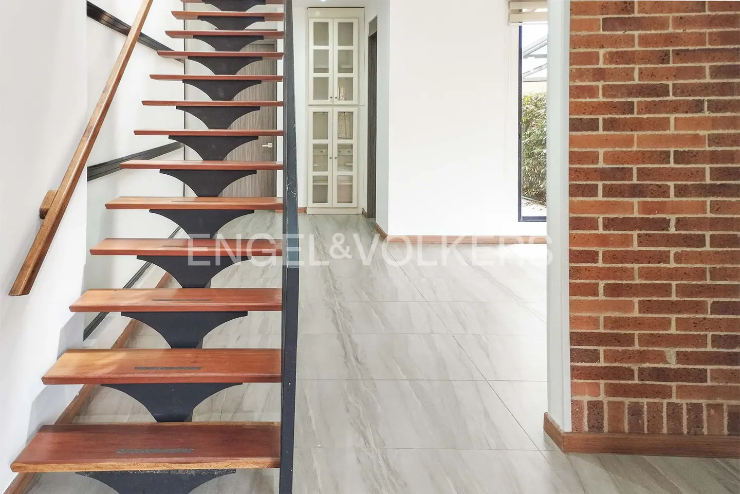 Interior view of a home featuring a wooden staircase, marble floors, a brick wall, and a white cabinet.